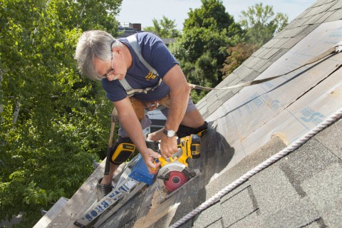 Man sawing skylight opening on a roof