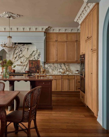 A bespoke kitchen with ornate trim, a chandelier flanked by a decorative ceiling medallion, and a light blue statement range hood