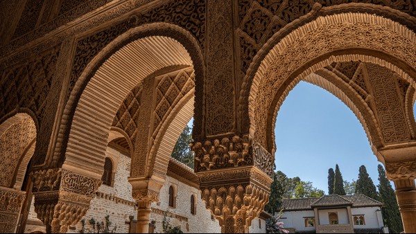 A detailed view of some of the arches of the Alhambra palace, with the sky visible in the background.