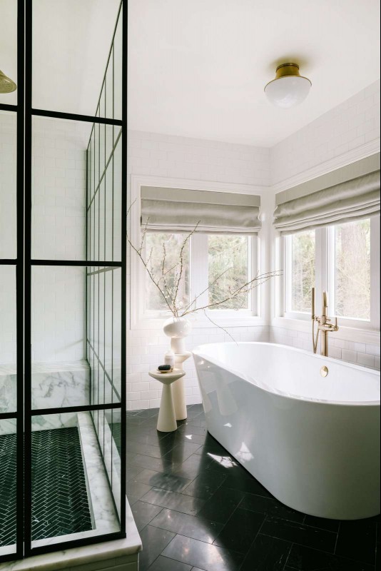 Jessica Nelson Design bathroom with white freestanding tub, black floor tile, and black framed glass shower box.