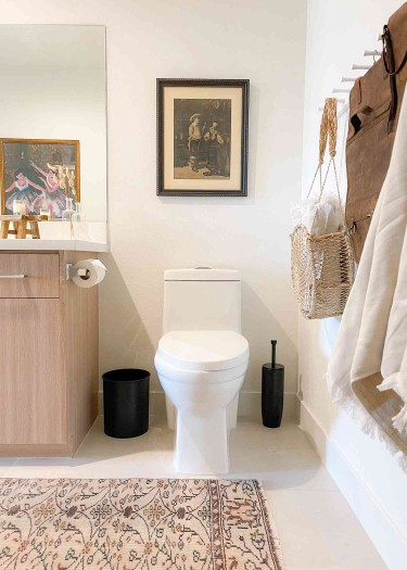 A modern-meets-vintage neutral bathroom featuring a patterned area rug and two vintage photo frames