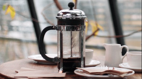 A Breakfast table with a French Press partway filled with coffee.