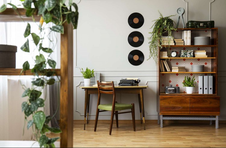 Black retro typewriter on a unique wooden desk, a mid-century modern chair and a renovated bookcase in a hipster home office interior.
