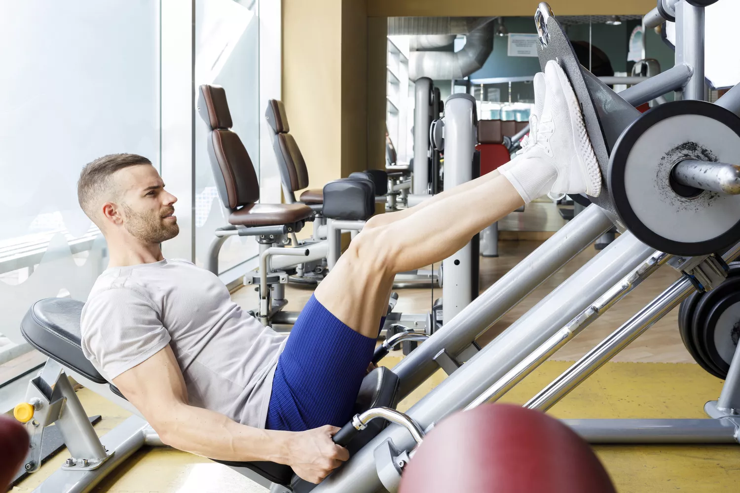 Young man exercising on leg press machine at gym