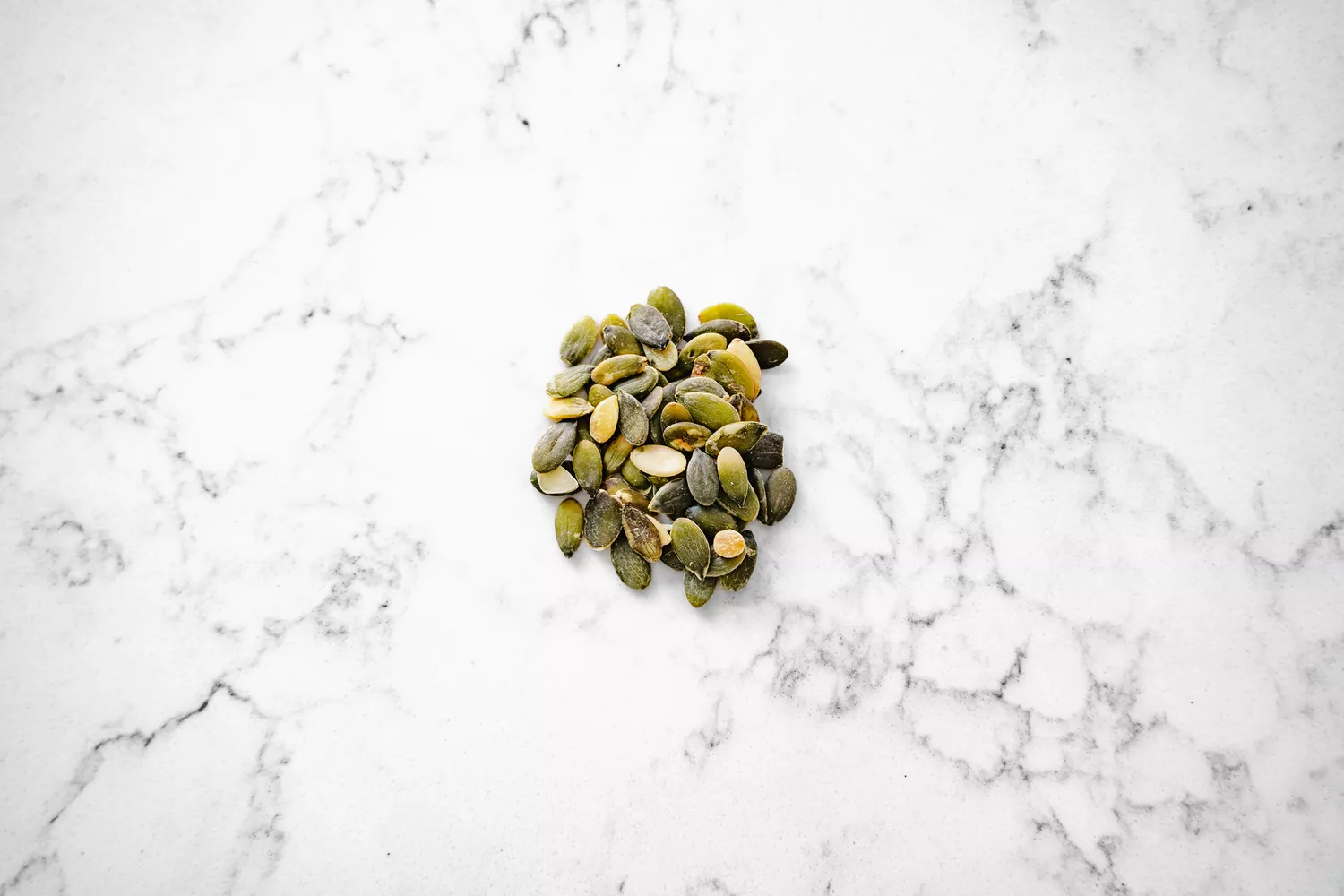 A small pile of pumpkin seeds on a marble surface.