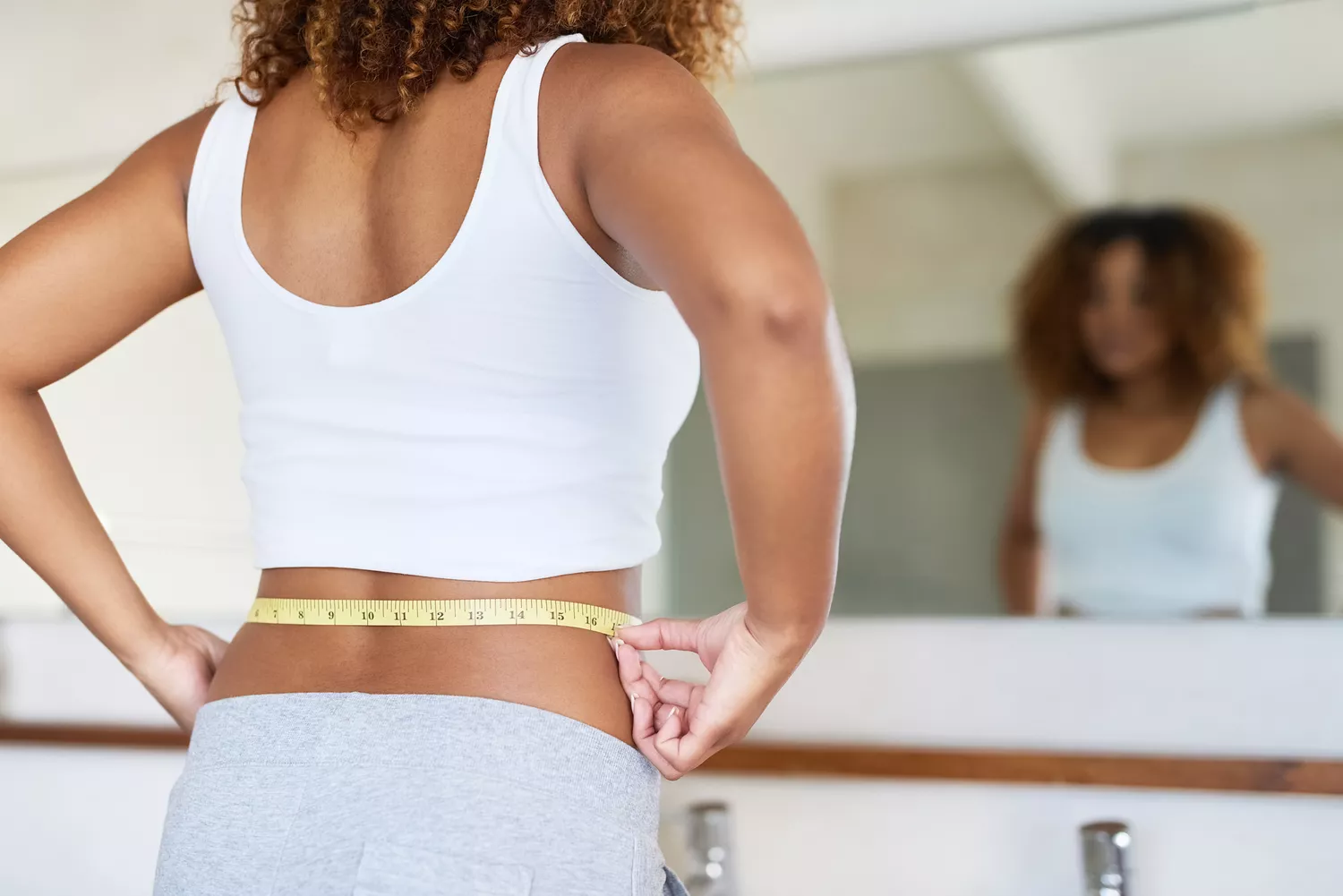 Cropped shot of a young woman measuring her waist in the bathroom