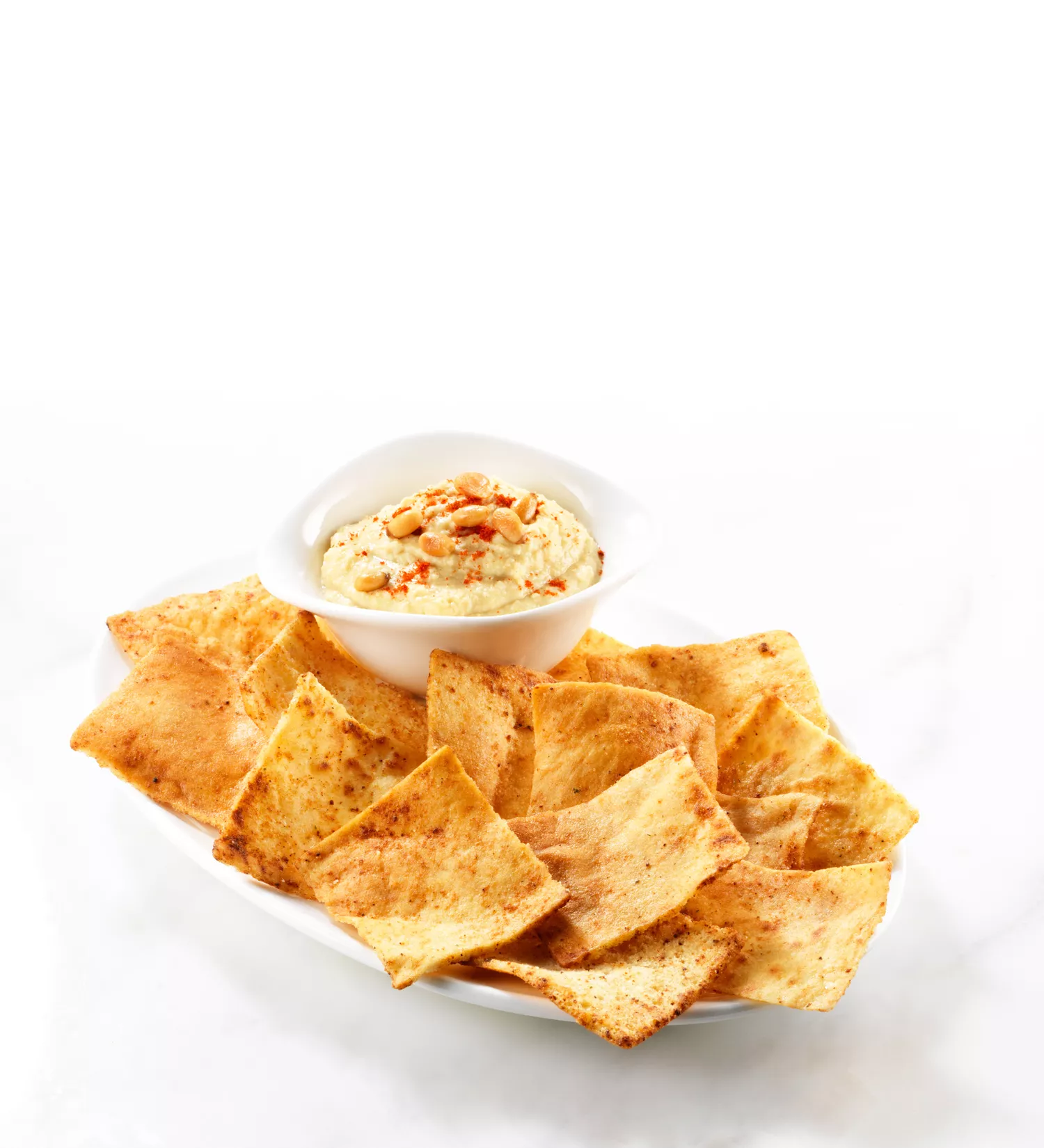 Pita chips in a shallow dish with a side of hummus topped with garnish.