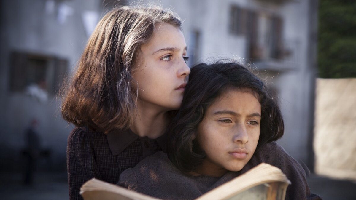 A still from the Italian TV show My Brilliant Friend featuring Elena and Lila as children reading together.