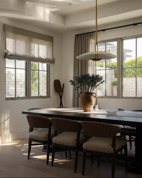 Modern rustic dining room with industrial modern pendant light, farm table, rattan wrapped dining chairs, and stone urn filled with thistle