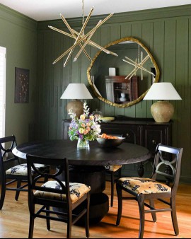 Moss green dining room with paneling, modern starburst brass chandelier, organic modern brass mirror, urn lamps, and black wood dining set