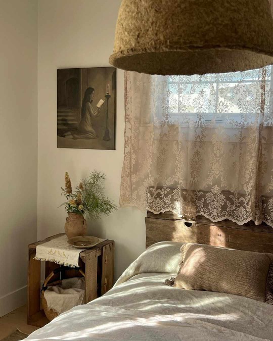 Country bedroom with lace curtains and rustic wood nightstand and headboard 