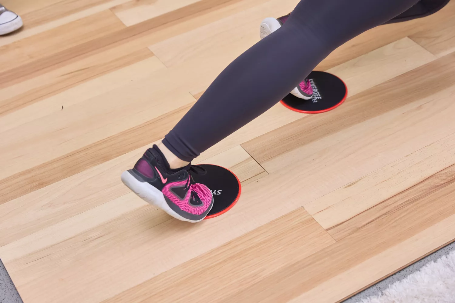 feet wearing sneakers and placed on each Synergee Core Slider set on wood floor 