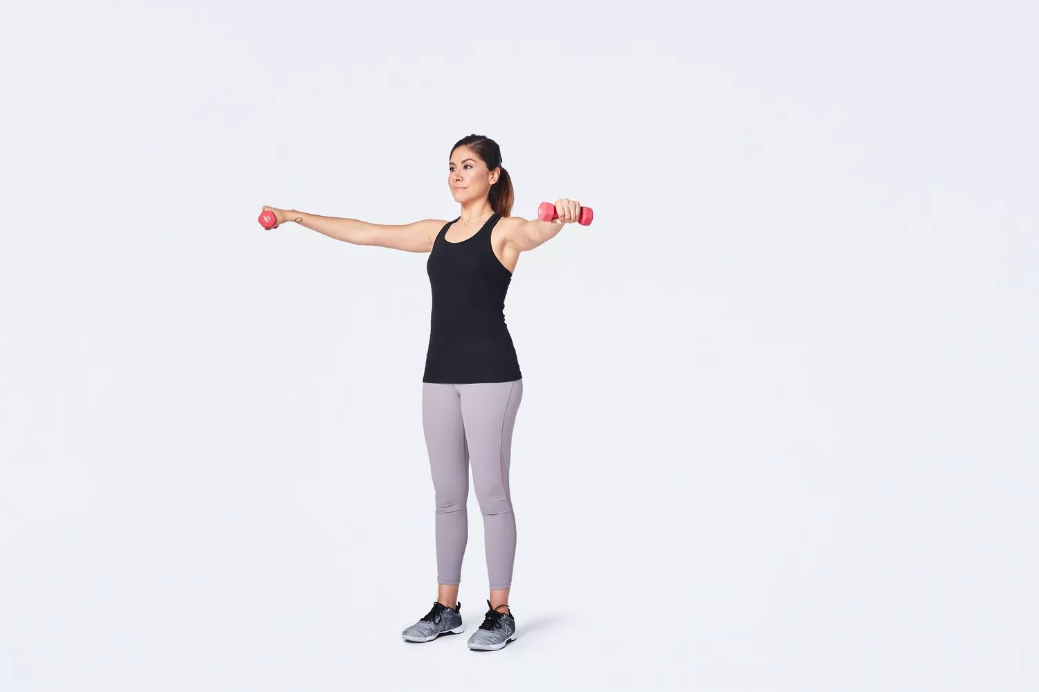 Standing woman lifting dumbbells to the side with both arms