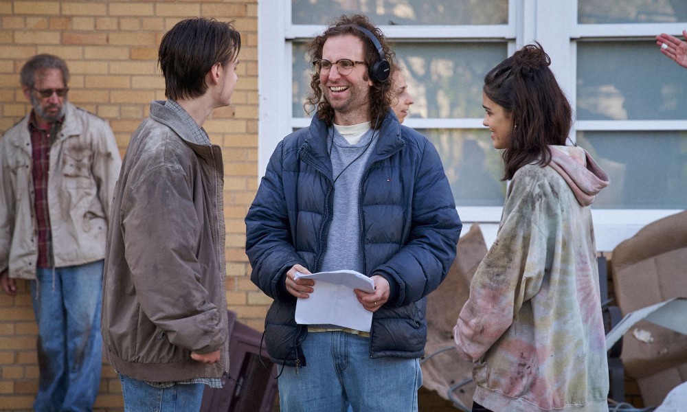 A man with headphones on stands between a boy and a girl in Y2K.