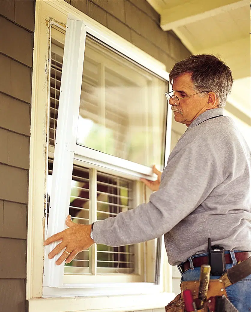 Image of Tom Silva installing storm windows on a home, making sure to center it in the window opening. 