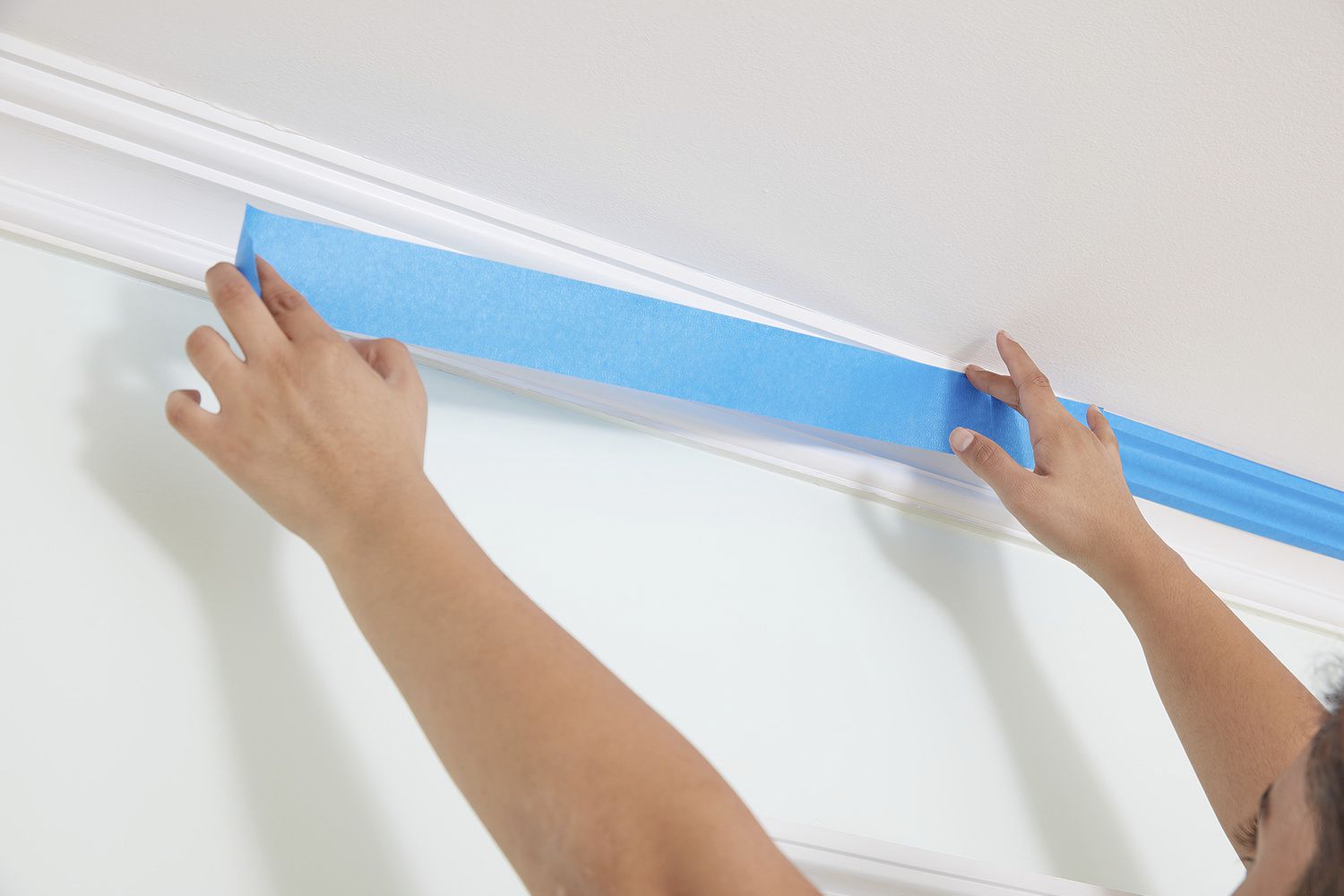 A person applying painters tape onto crown molding. 