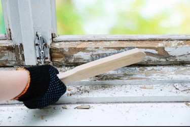 Brush with metal bristles in hand to remove old paint from the window.