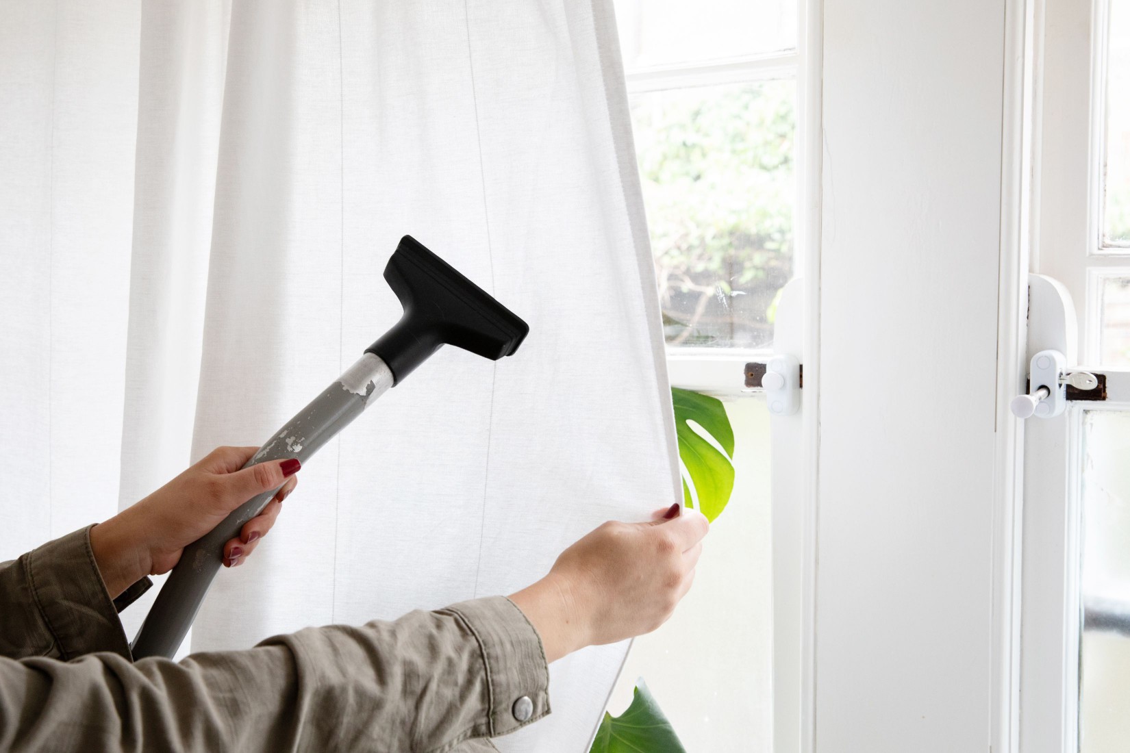 Vacuum hose removing dust and cat dander from white curtains