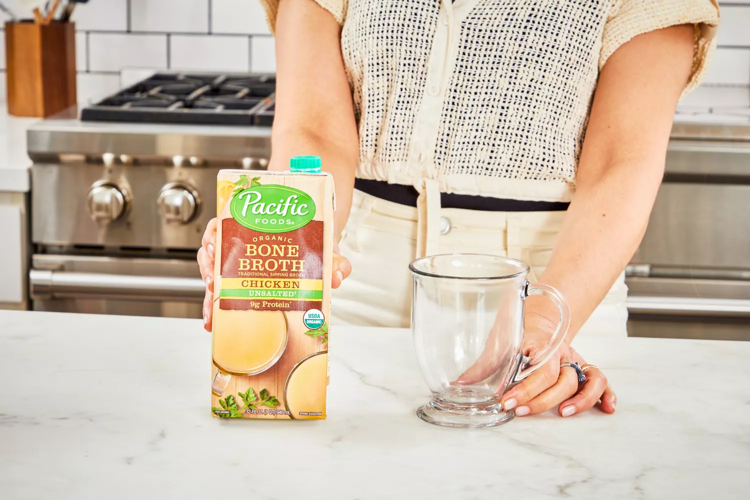 A person holds a box of Pacific Foods Chicken Bone Broth 
