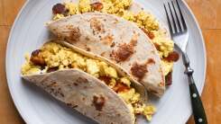 Top-down photo of two breakfast tacos in flour tortillas on a white plate.
