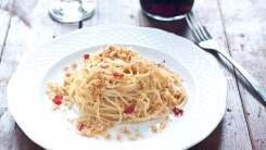 A photograph of spaghetti topped with breadcrumbs and dried red chili flakes on a white plate.