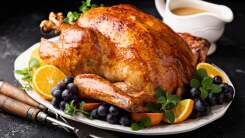 A cooked turkey on a platter surrounded by a gravy boat and utensils