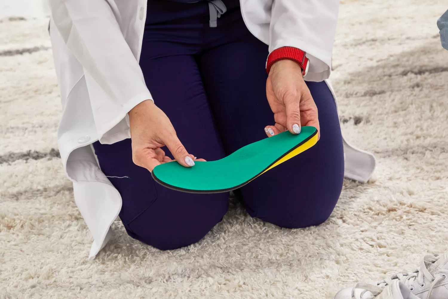 A person holding a Spenco PolySorb Cross Trainer Insoles while kneeling on a rug 