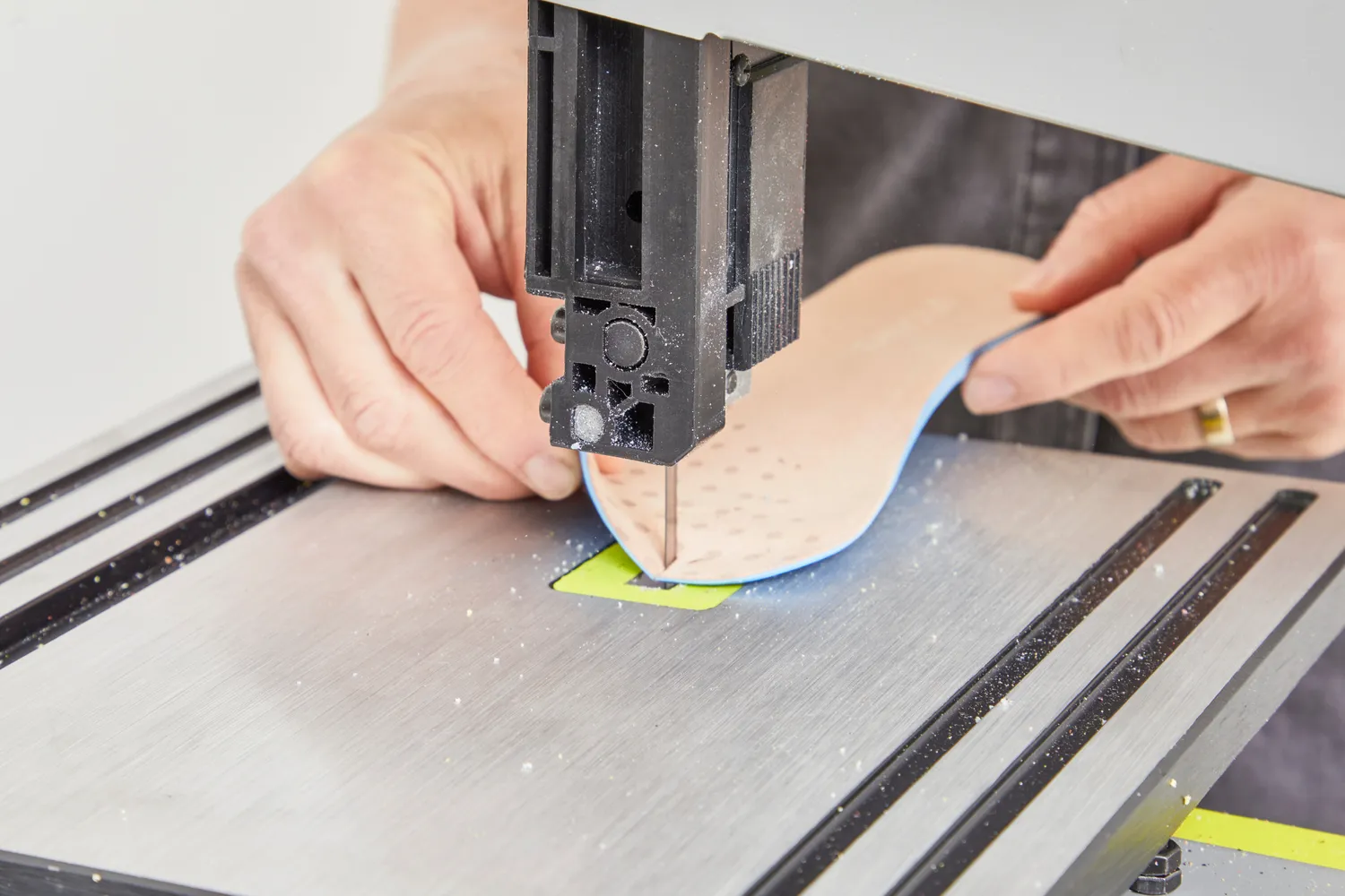 Hands cutting a Vionic Slimfit Orthotic Insole in half with a band saw
