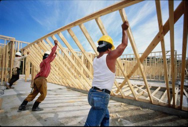 construction workers lifting up wooden frame of house
