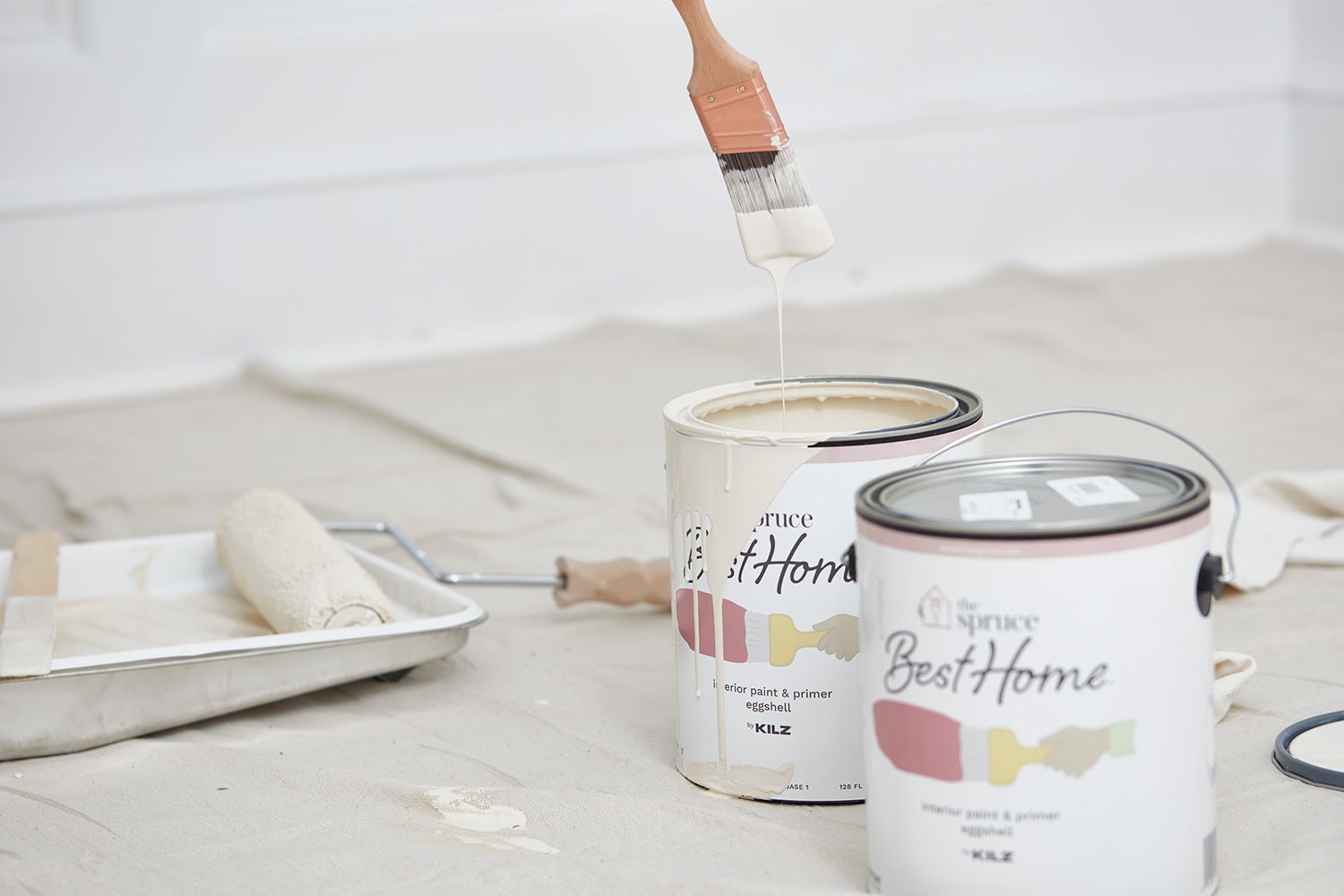 Paint brush dipped in Spruce paint buckets with cream-colored paint for interior walls