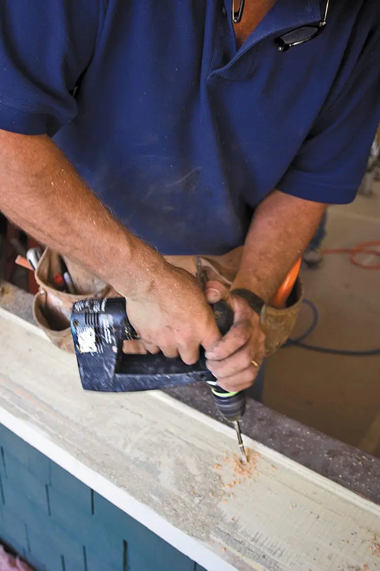 A man drills into the window sill to prepare for replacement windows.