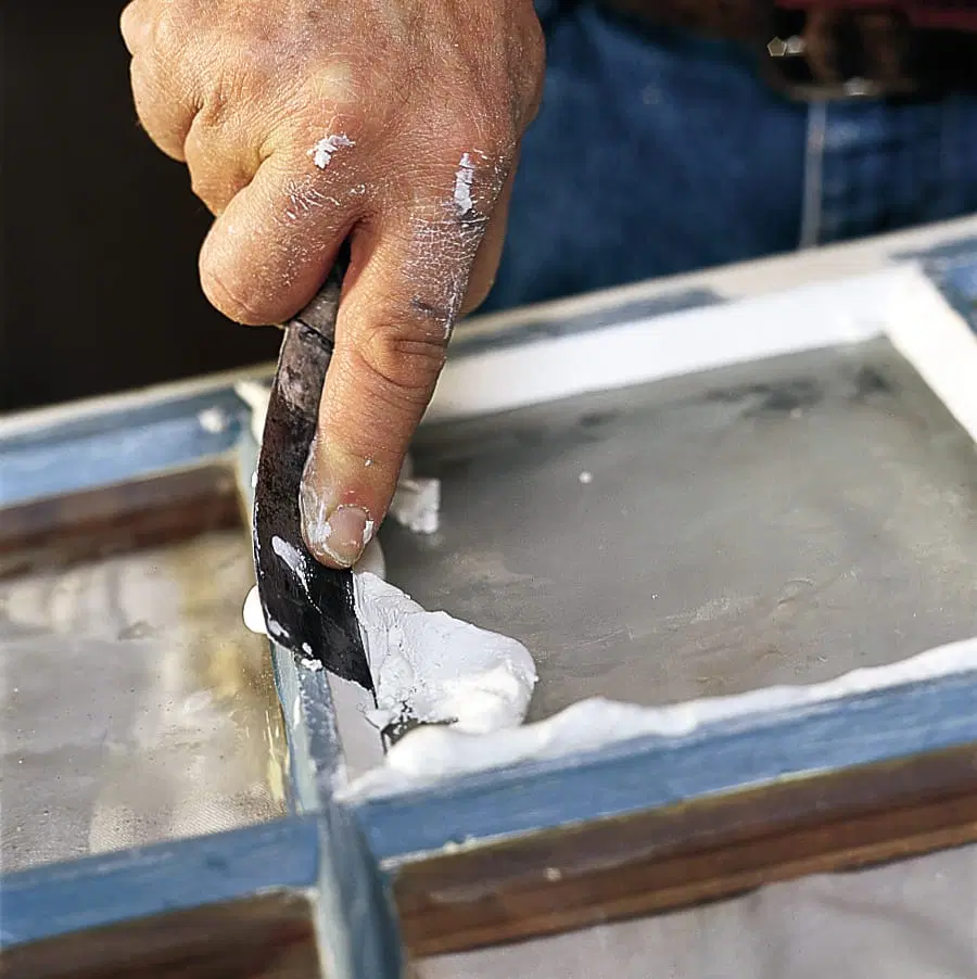 A putty knife being used to smooth the putty on the surface of a window pane.