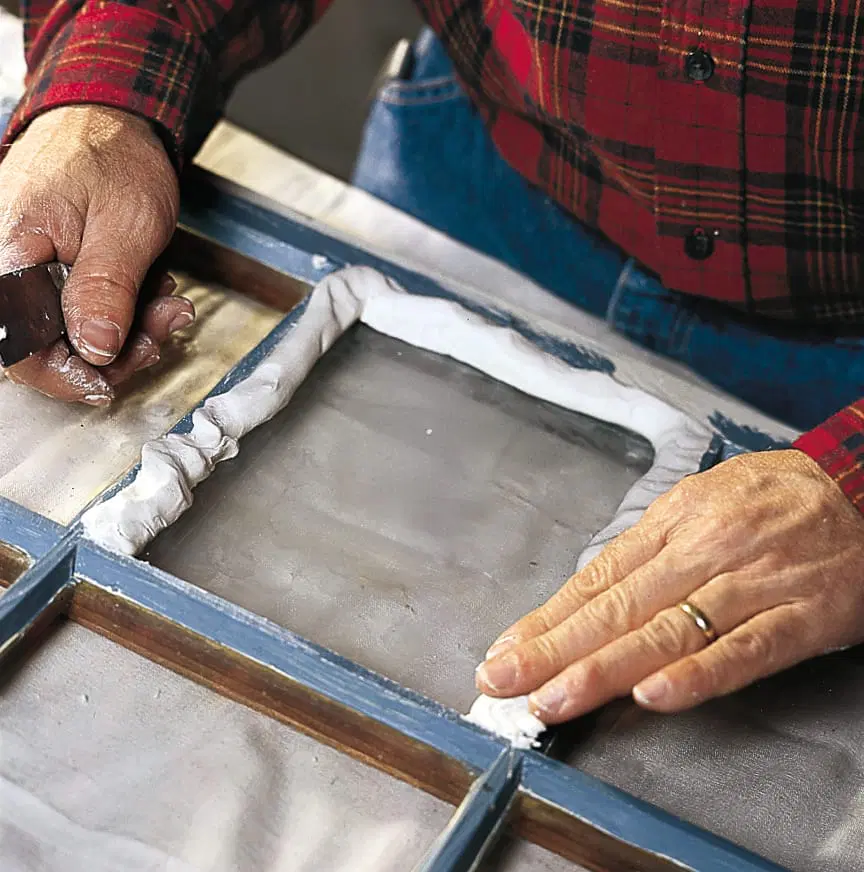 A man applying a putty rope to the inside of a window pane.