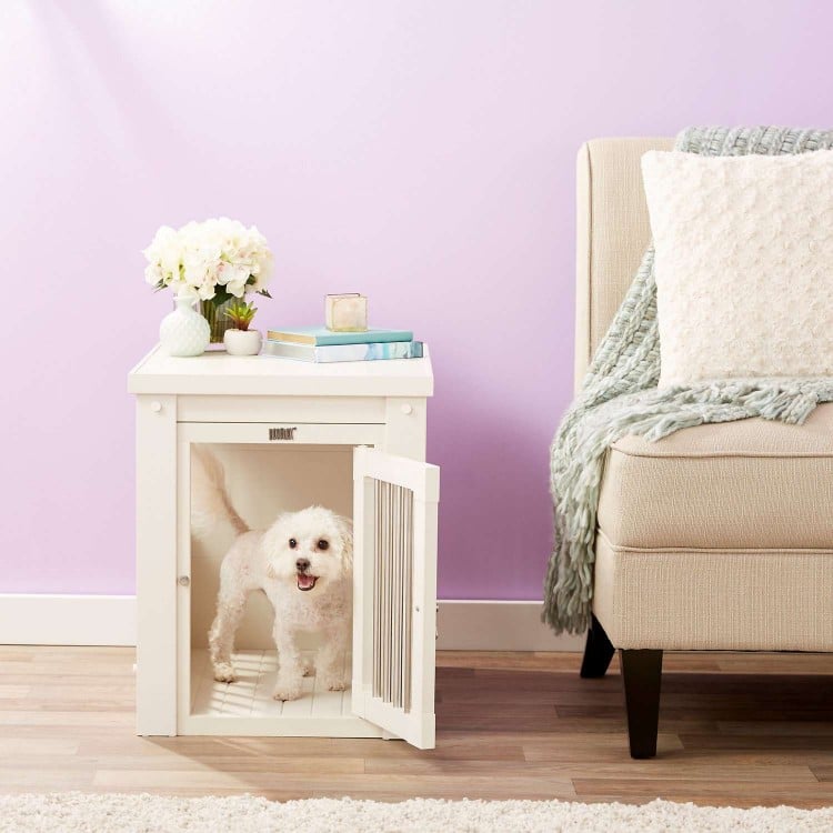 Furniture-style dog crate with a white dog inside in a living room