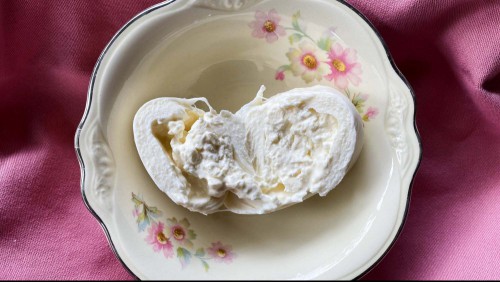 Cross section of burrata cheese in a bowl on a mauve napkin