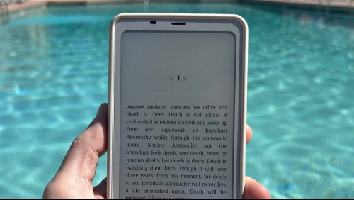 A book open on the Boox Palma, held in one hand with a pool visible in the background