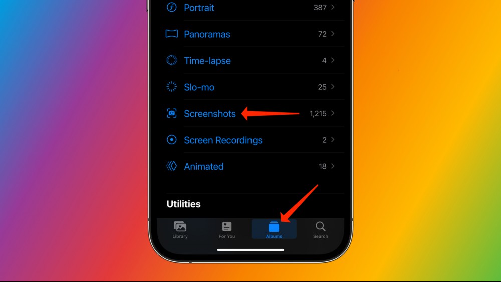 An iPhone against a rainbow background, with the Photos app open. Two arrows are pointing to the Albums tab and the Screenshots album respectively.