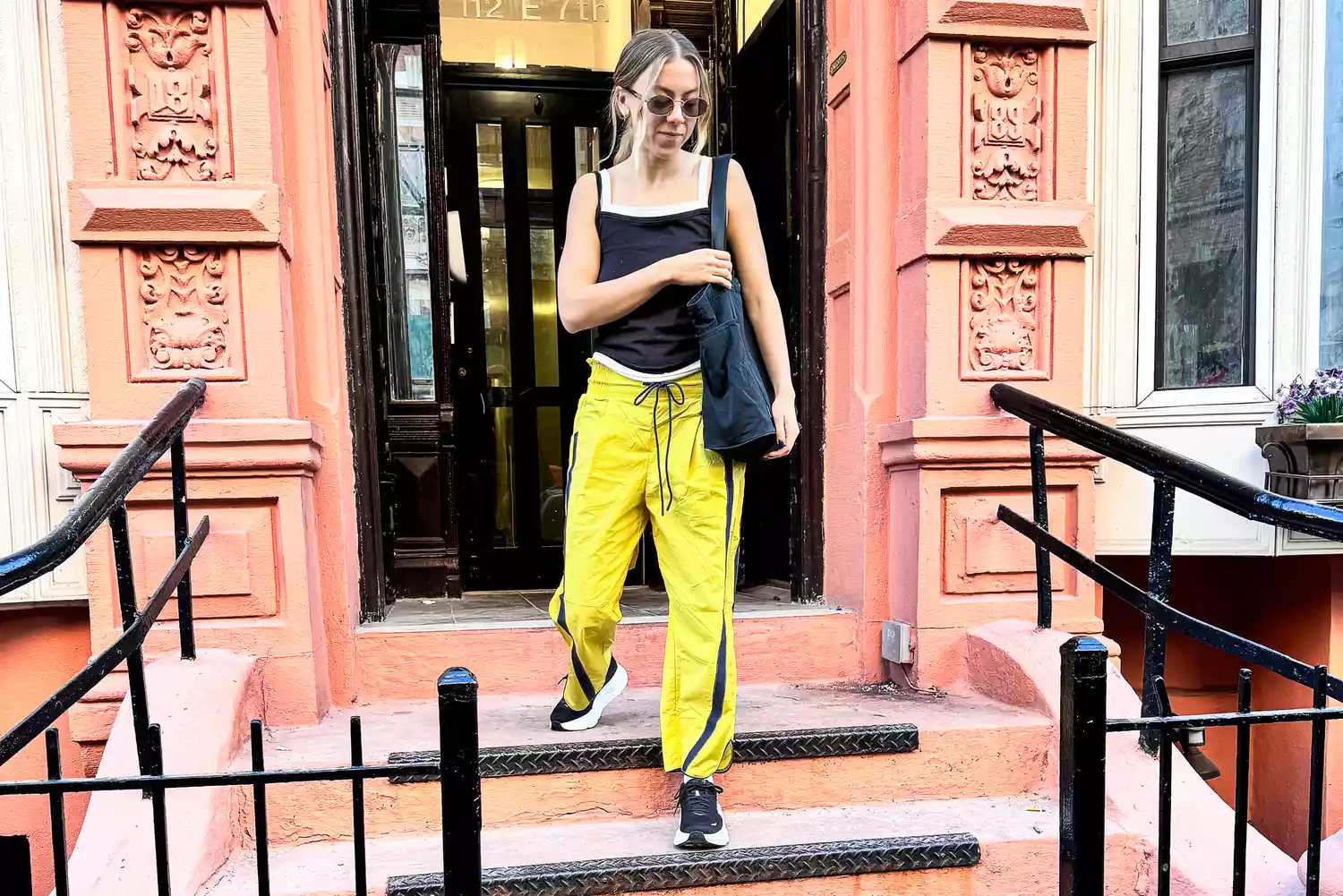 A woman wears a black tank top, Free People Champ Is Here Pants, and Hoka Bondi 9 sneakers