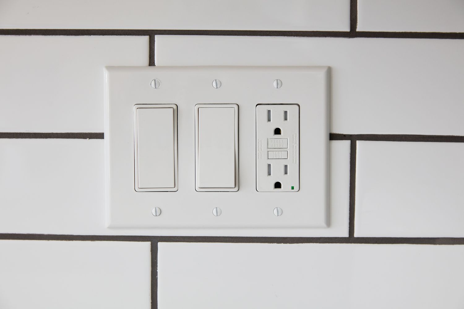 Kitchen outlet with two white switches on tiled wall