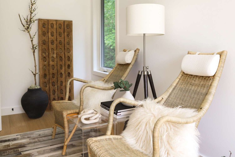 Neutral wooden chairs with faux sheepskin pillows on top next to lamp and side table with books