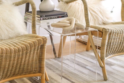 Glass side table with decorative sculpture next to stacked books and wicker chairs