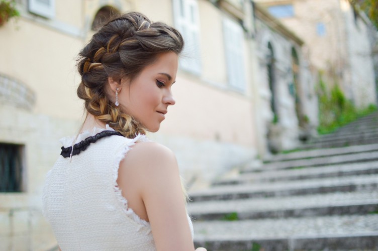 A woman standing outside an outdoor stairwell with a French braid in her hair.