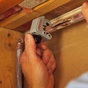 A miniature tubing cutter being used to slice through a copper water pipe.