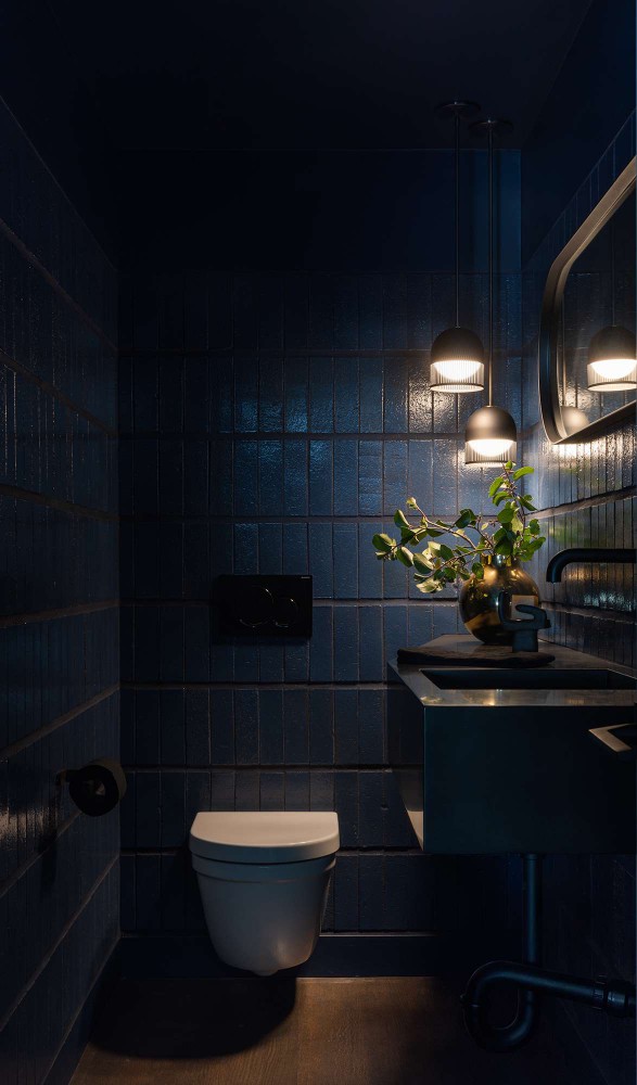 Regan Baker Design moody masculine power room with dark blue tiles and black fixtures.