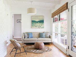 Home addition with ceiling to floor windows next to couch and Moroccan pouf in center
