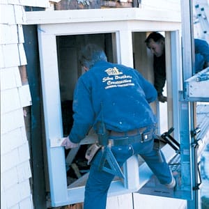 2 Men installing a bay window into the second story of a home.