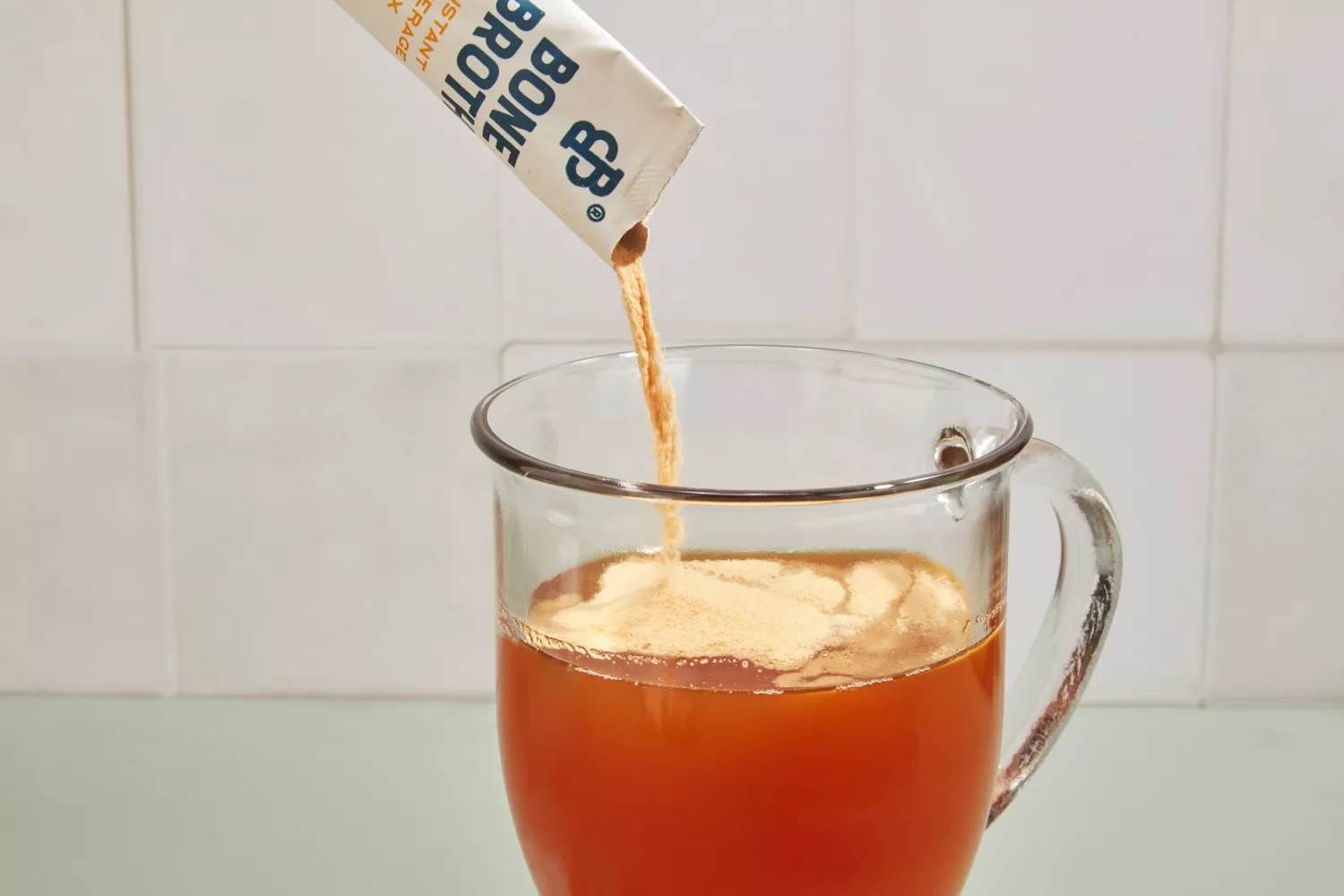 A packet of Bare Bones Bone Broth Instant Powdered Beverage Mix is poured into water