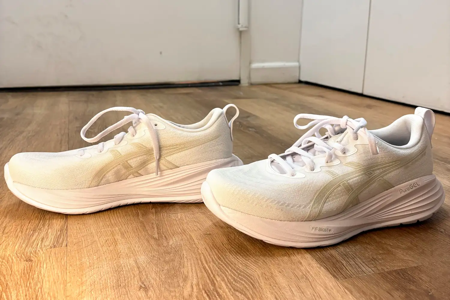 A pair of Asics Women's Gel-Cumulus 27 Running Shoes on a wooden floor