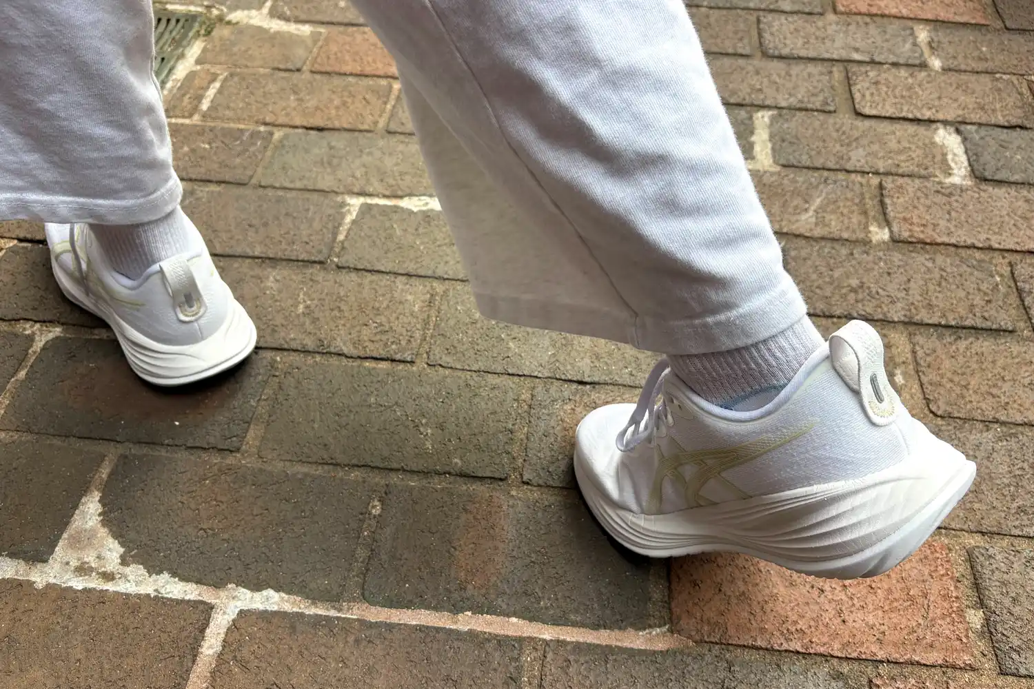 A person walks outside on brick while wearing the Asics Women's Gel-Cumulus 27 Running Shoes