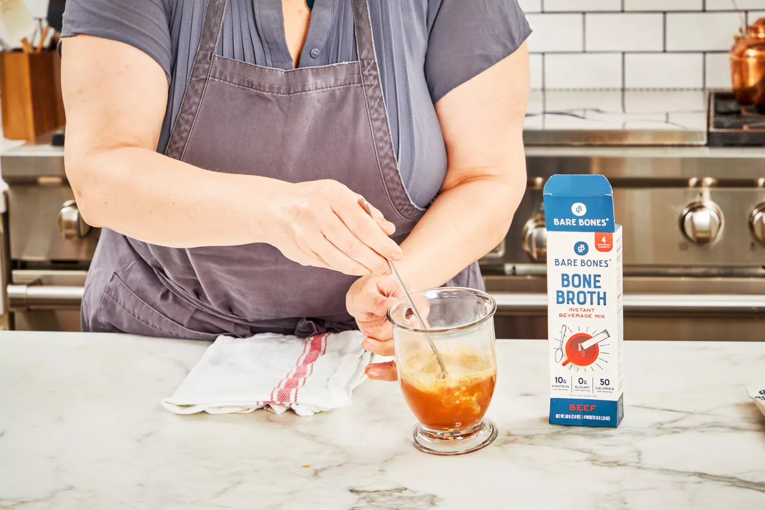 A person stirs a glass of Bare Bones Bone Broth Instant Powdered Beverage Mix